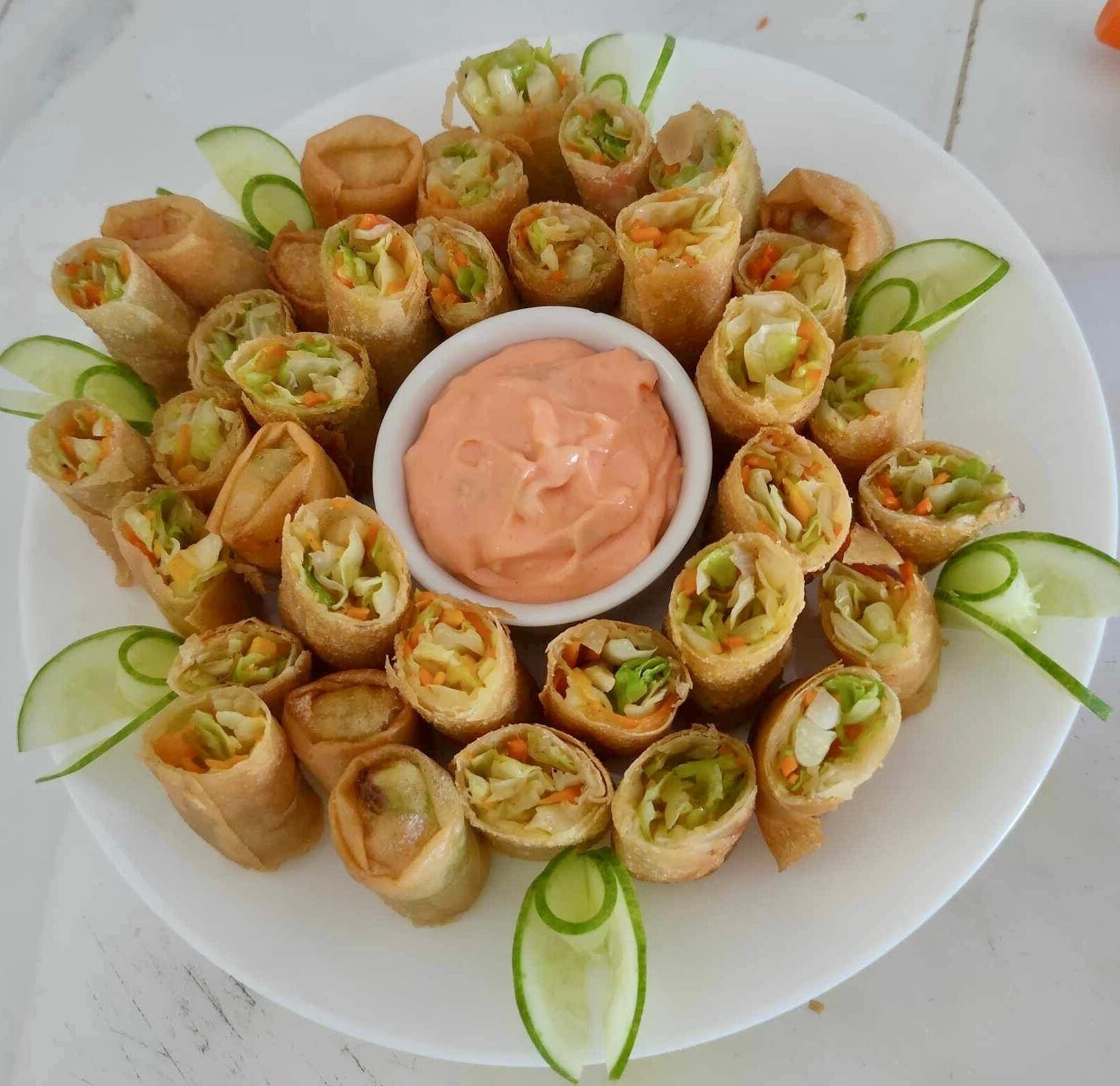 Une assiette de rouleaux de printemps, accompagnés d’une sauce pour tremper et de tranches de concombre.