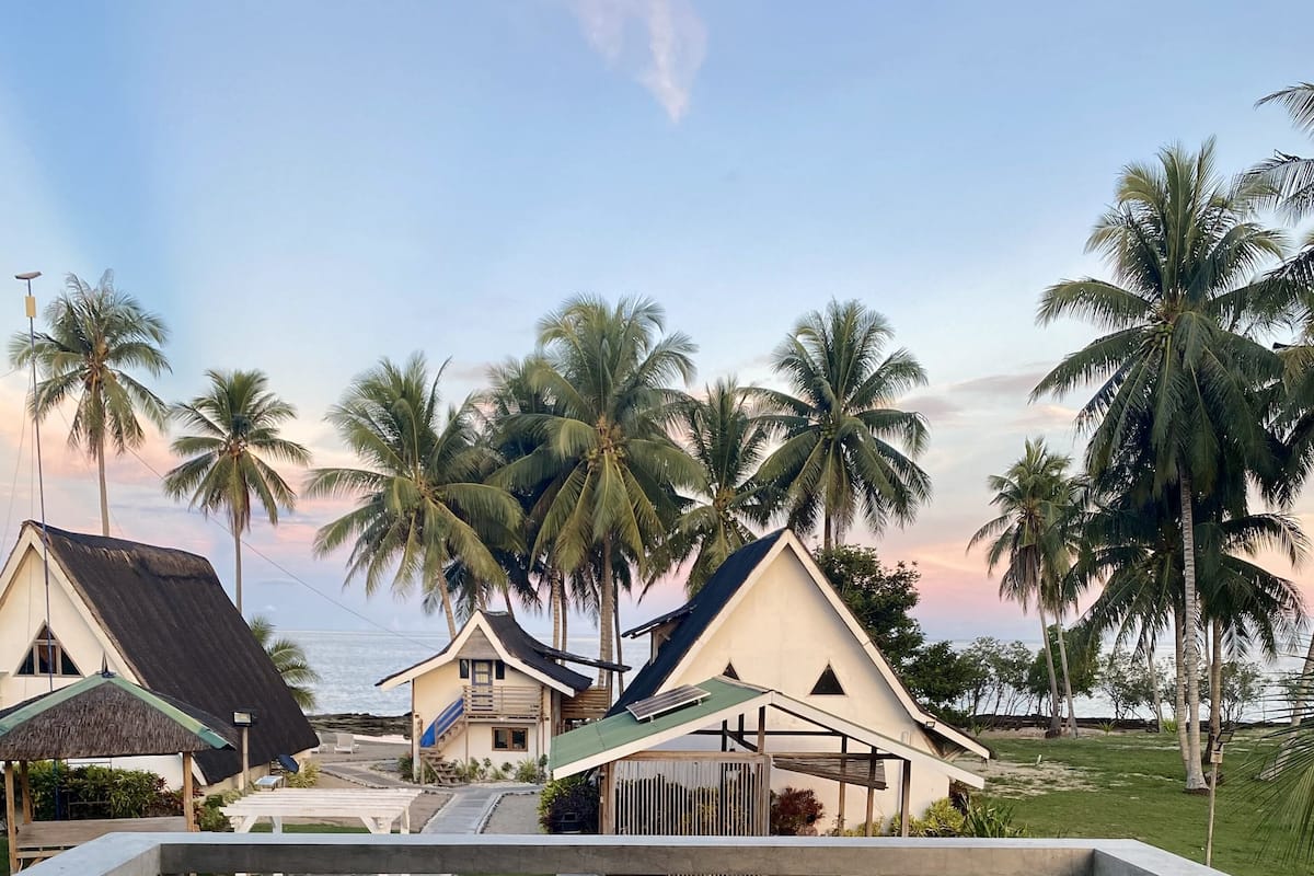 A balcony with two chairs and a table, overlooking a resort area with palm trees and buildings.