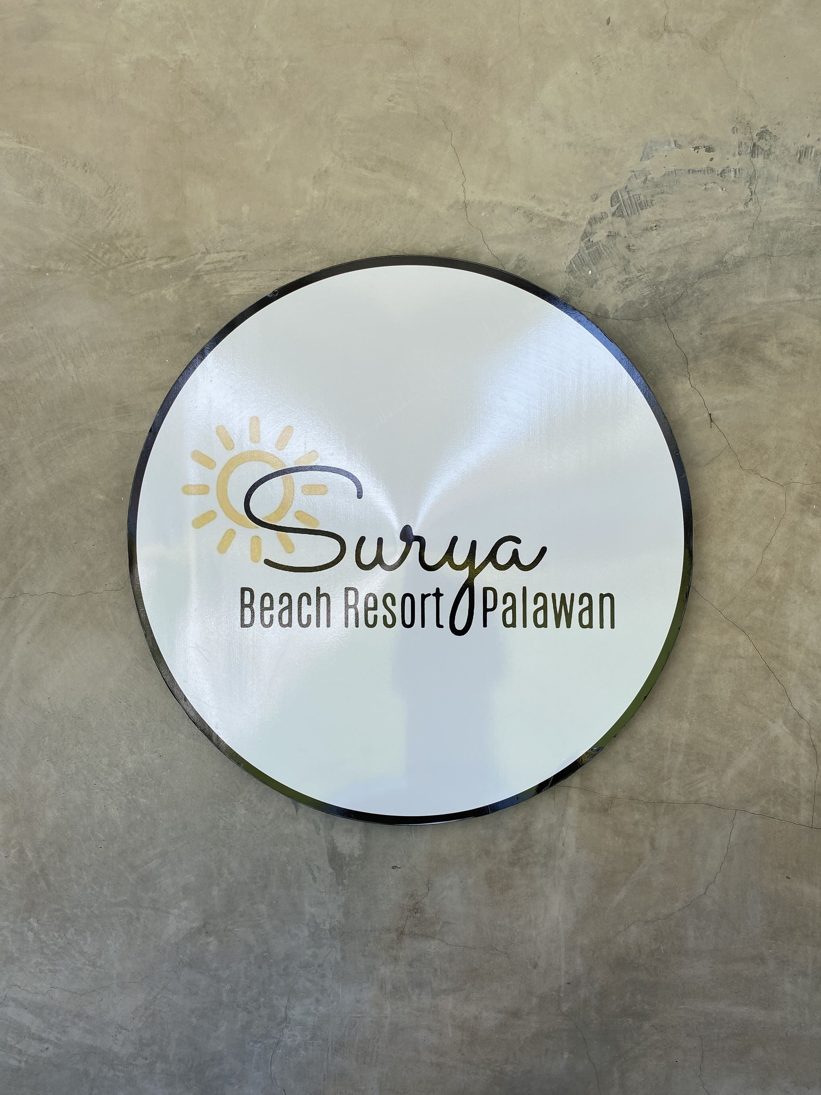 Een rond bord met de tekst 'Surya Beach Resort Palawan' en een zon-pictogram.