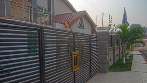 A gated entrance with a metal gate, a small yellow sign, and a flagpole with a flag. - Labev Hotel (Kumasi)