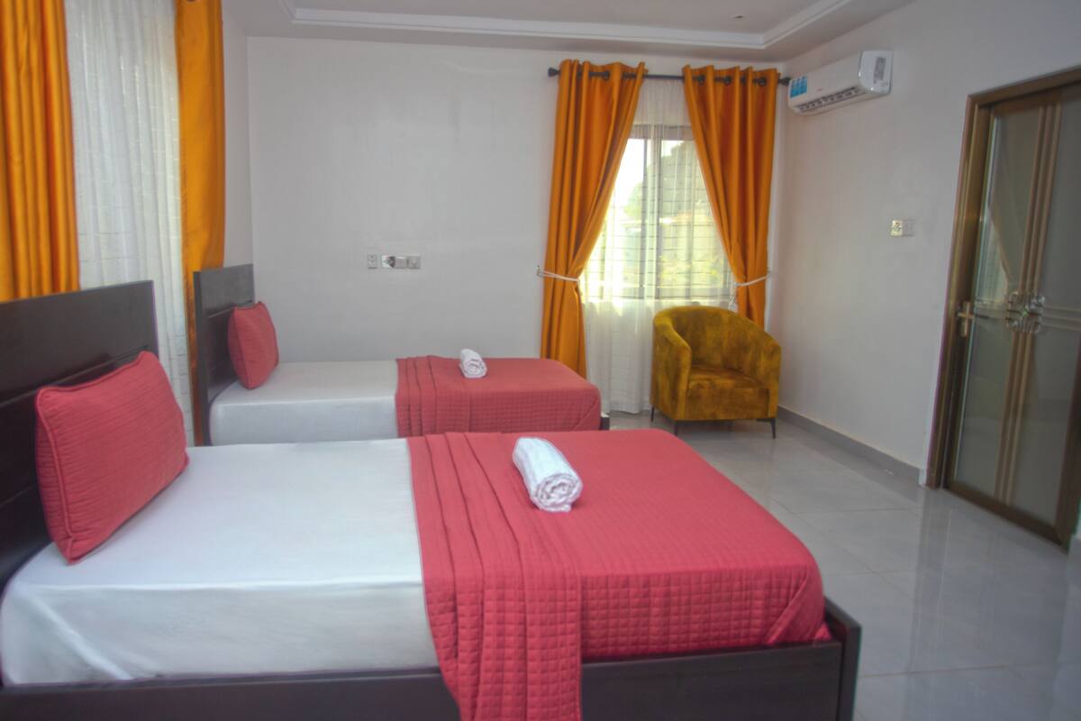 A hotel room with two beds, a chair, and a sliding door.