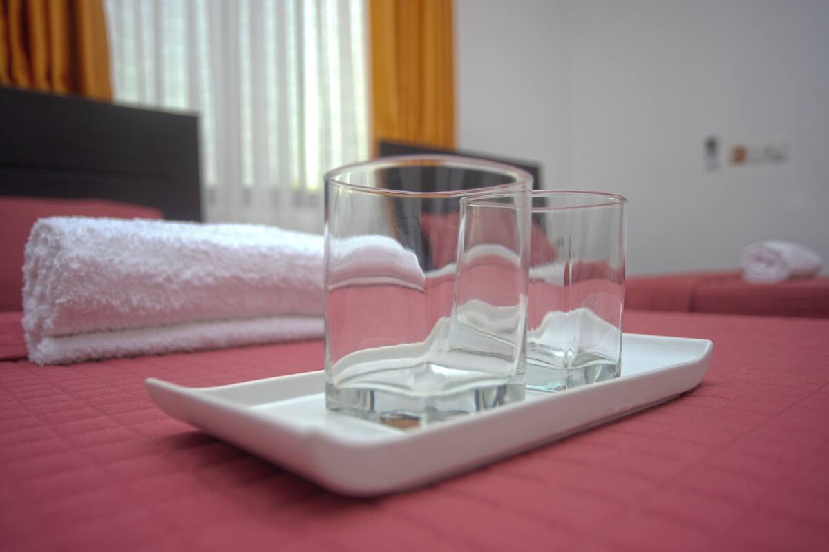 A bed with a white towel and two clear glasses on a white tray.