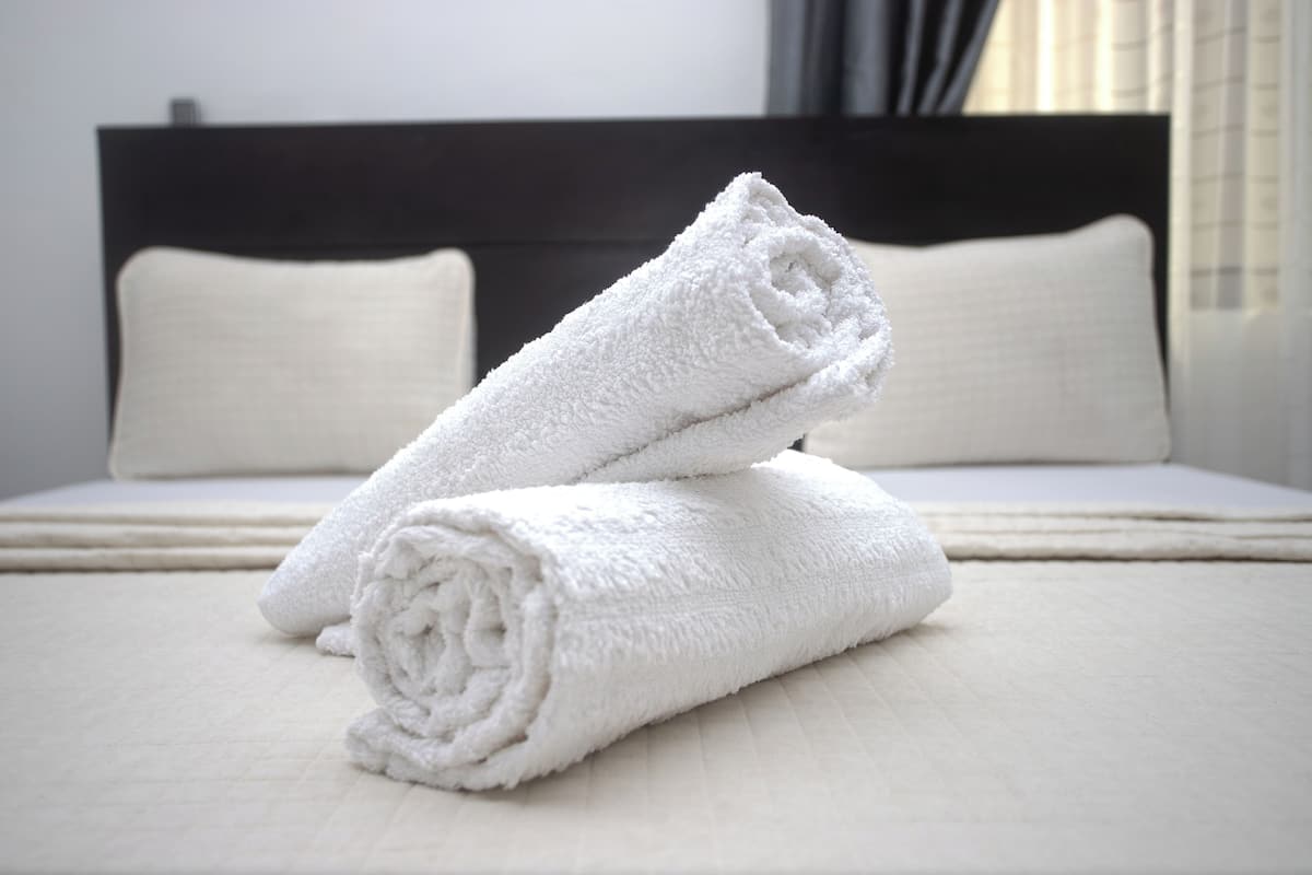 A neatly made bed with white linens and pillows, a dark headboard, and a window with curtains.