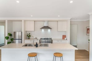 Une cuisine moderne dotée d’un îlot central, d’appareils électroménagers en acier inoxydable et d’un dosseret de carrelage blanc.
