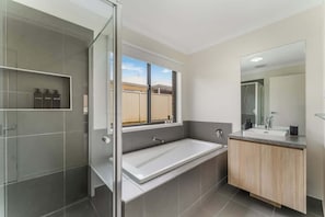 A modern bathroom with a glass shower enclosure, a large bathtub, and a vanity with a mirror. - Living The Dream At Lyric Crt (Canadian)