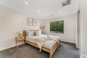 Une chambre à coucher avec un lit, une table de chevet, une lampe, une fenêtre et des œuvres d’art murales.