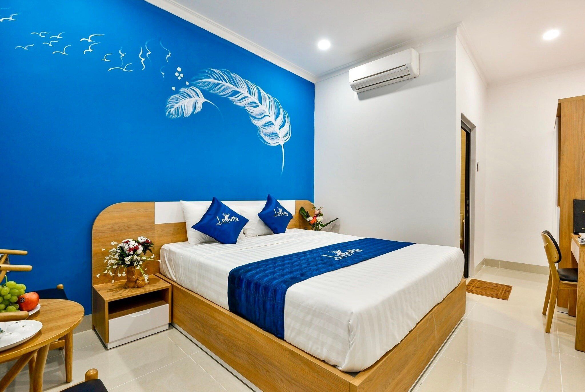 A hotel room with a bed, a wooden nightstand, a desk, and a chair.