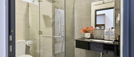 A modern bathroom with a glass-enclosed shower, a toilet, a sink with a mirror, and a vase with flowers.