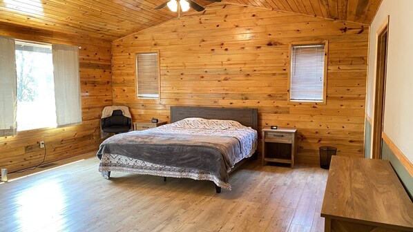 Une chambre dans une cabane en bois, comprenant un lit, une table de chevet, une chaise et une fenêtre avec des stores.
