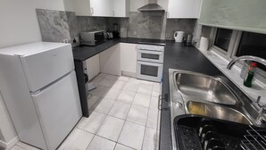 Una cocina moderna con armarios blancos, encimera negra, horno empotrado, microondas y pileta de acero inoxidable.