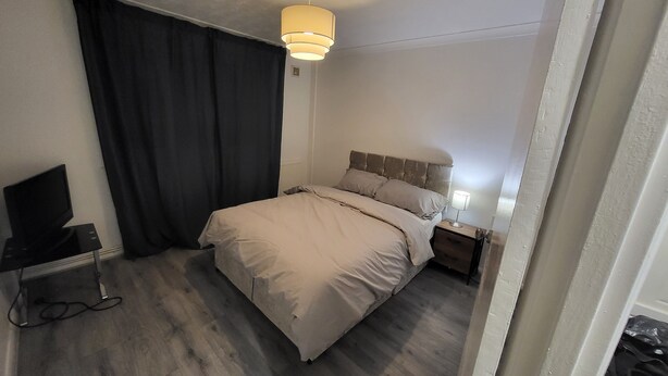 A hotel room with a bed, a TV, a bedside table, and a lamp.