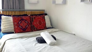 A neatly made bed with striped bedding, two red patterned pillows, and a rolled towel.