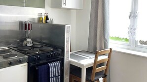 A compact kitchen with a stove, oven, and a small dining table with a chair.