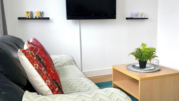 A modern living room with a sofa, a television mounted on the wall, and a small wooden side table with a plant.