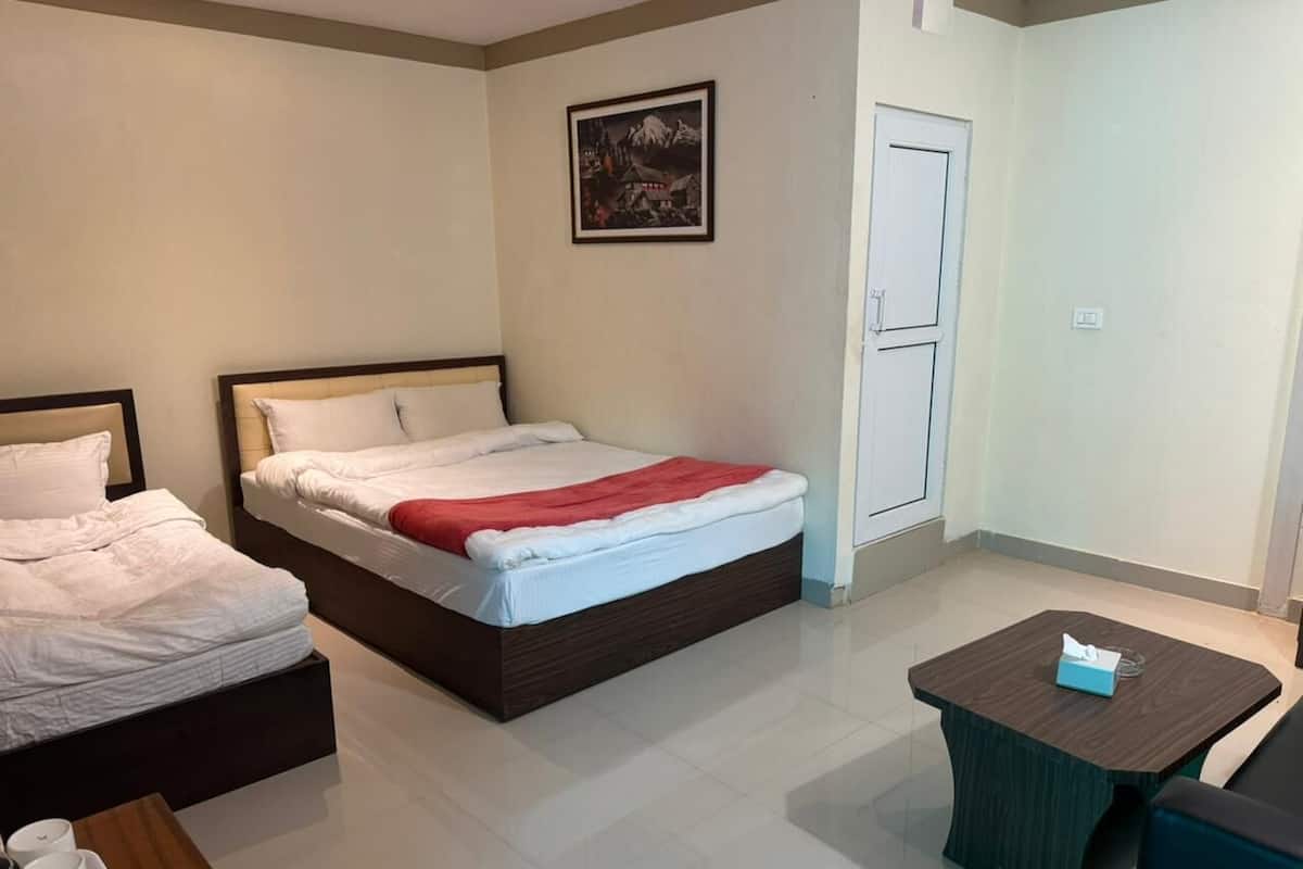 A hotel room with two beds, a small table, and a door.