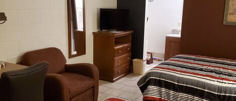 A bedroom with two beds, a desk, a chair, a dresser, and a television.