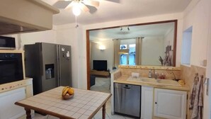 A compact kitchen with a refrigerator, a microwave, a sink, and a dining table with a fruit bowl.
