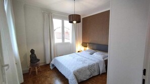 Un dormitorio con una cama, una mesita de noche, una lámpara, una ventana con cortinas y una estatua.