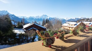 A wooden balcony with a view of snow-covered mountains and houses.
