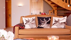 A cozy living room with a brown sofa, two decorative pillows with deer images, a glass candle on a wooden table, and a magazine.