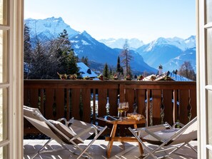 Un balcón con dos sillones, una mesita y vistas a montañas nevadas.