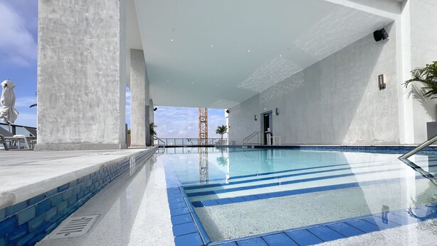 Une piscine intérieure moderne, avec une eau d’un bleu limpide, un sol carrelé et une vue sur le ciel.