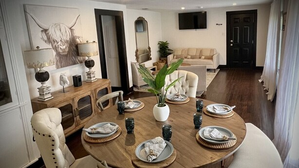Un comedor con una mesa redonda de madera, sillas blancas tapizadas y una planta en maceta.