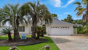 A single-story house with a garage, surrounded by palm trees and a well-maintained lawn. - Summer Available! Private Pool, Private Home 6min walk to the Beach! (Panama City Beach)