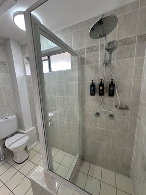 Een moderne badkamer met een douchecabine van glas, een toilet en twee flessen shampoo.