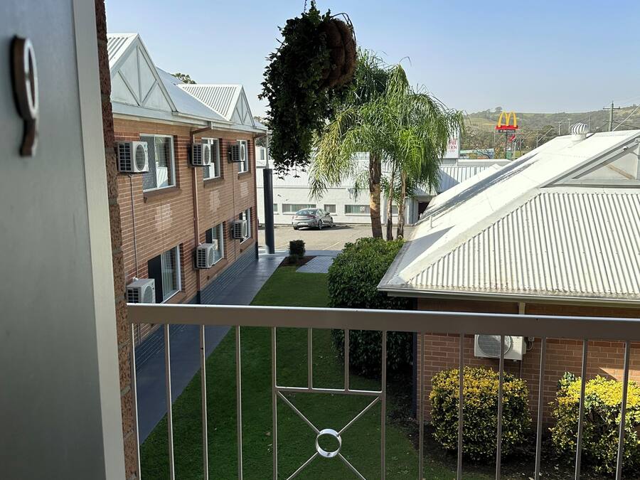Een balkon met uitzicht op een woongebied, met huizen inclusief airconditioners, een McDonald's bord en een hangplant.