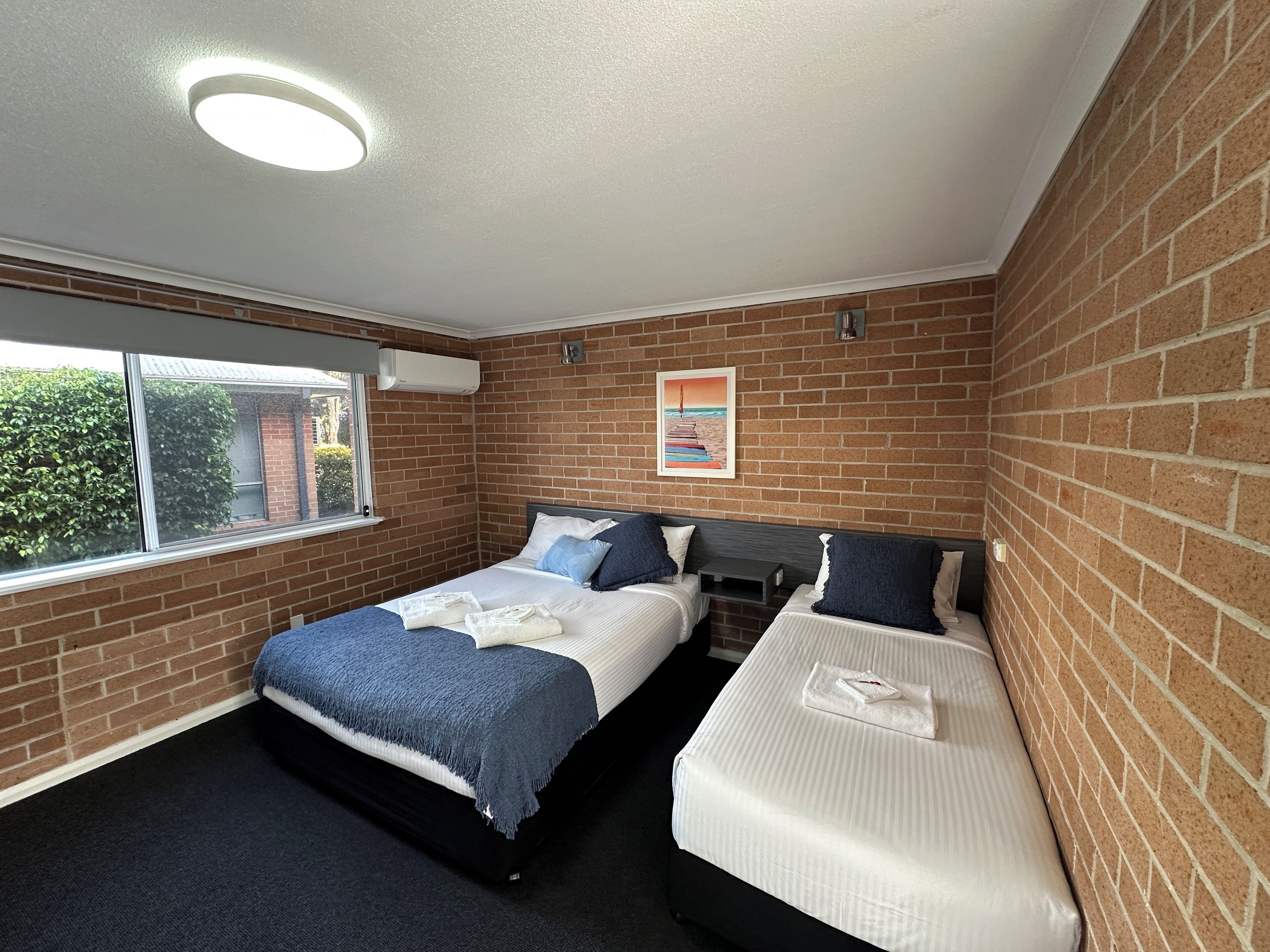 A hotel room with two beds, a window, a brick wall, and a ceiling light.