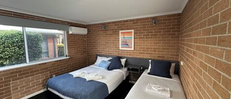 A hotel room with two beds, a window, a brick wall, and a ceiling light.