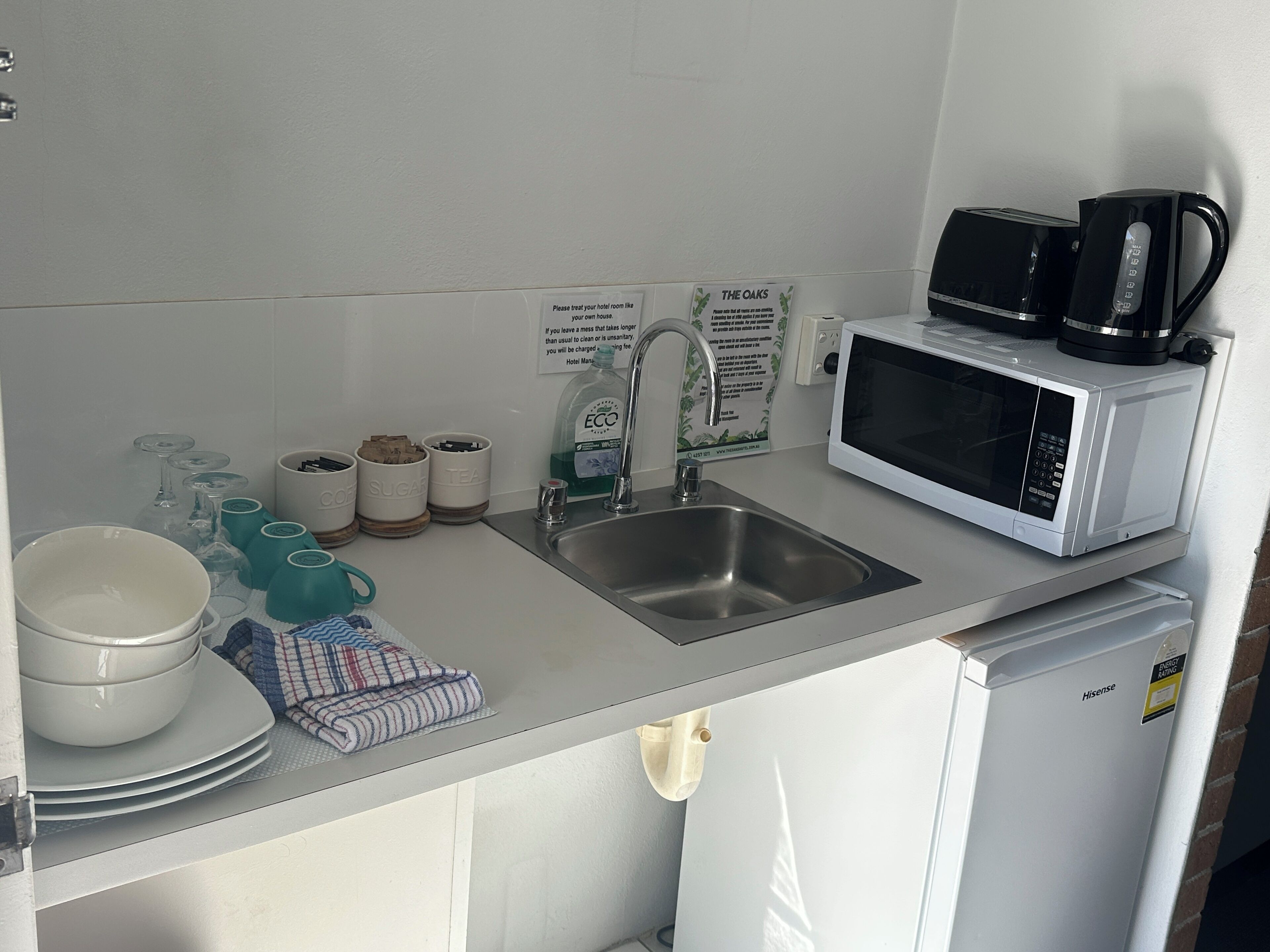 A kitchen with a sink, a microwave, and a coffee maker. There are cups and glasses on the counter.