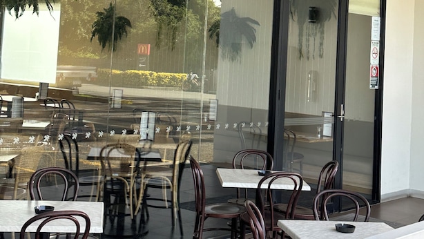 An indoor seating area with tables and chairs, large windows, and hanging plants.