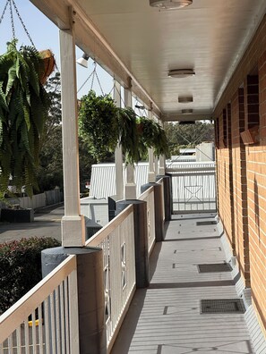 A covered outdoor area with hanging plants, a brick wall, and a white railing. - The Oaks Hotel Motel (Albion Park Rail)