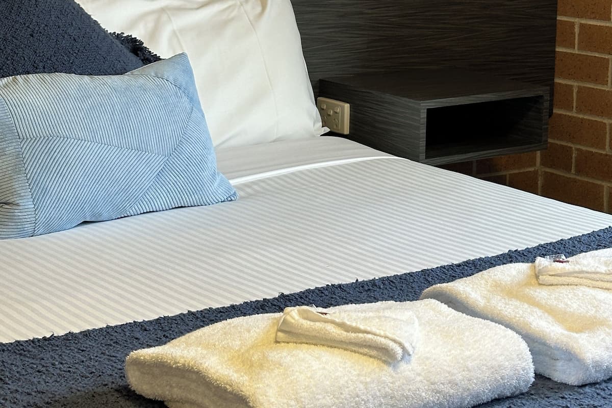 Ein Schlafzimmer mit Backsteinwand, einem Bett mit weißer und blauer Bettwäsche, einem dunklen Kopfteil und einem Gemälde über dem Bett.