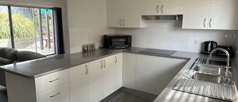 Una cocina moderna con armarios blancos, un lavamanos de acero inoxidable, un microondas y una cafetera.