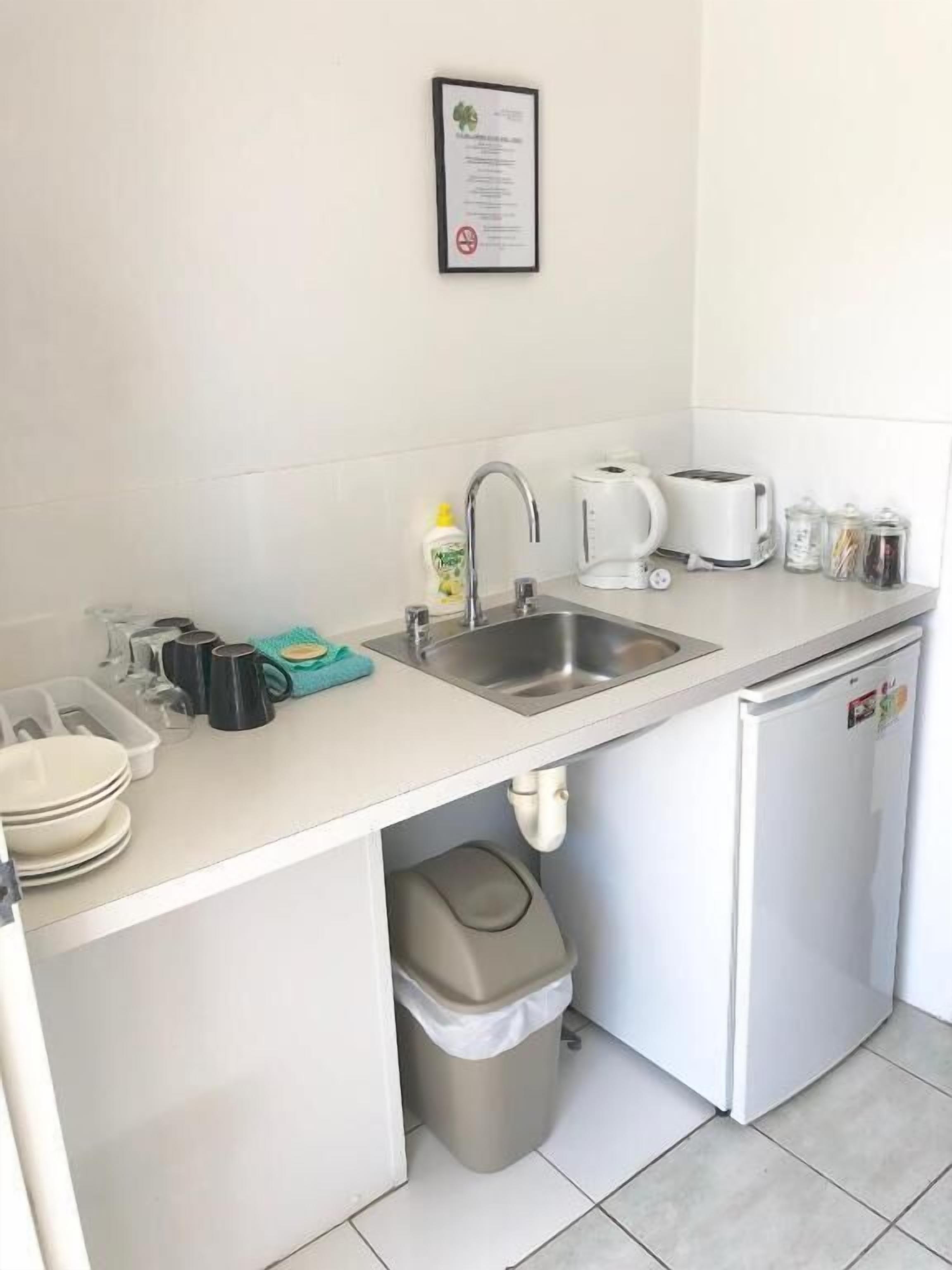 A compact kitchenette with a sink, a coffee maker, a toaster, and a trash bin.