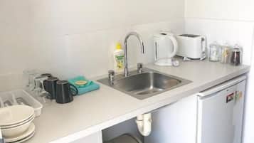 A compact kitchenette with a sink, a coffee maker, a toaster, and a trash bin.