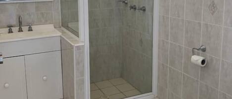Een badkamer met een douchecabine van glas, een toilet, een wastafel met spiegel en betegelde wanden.
