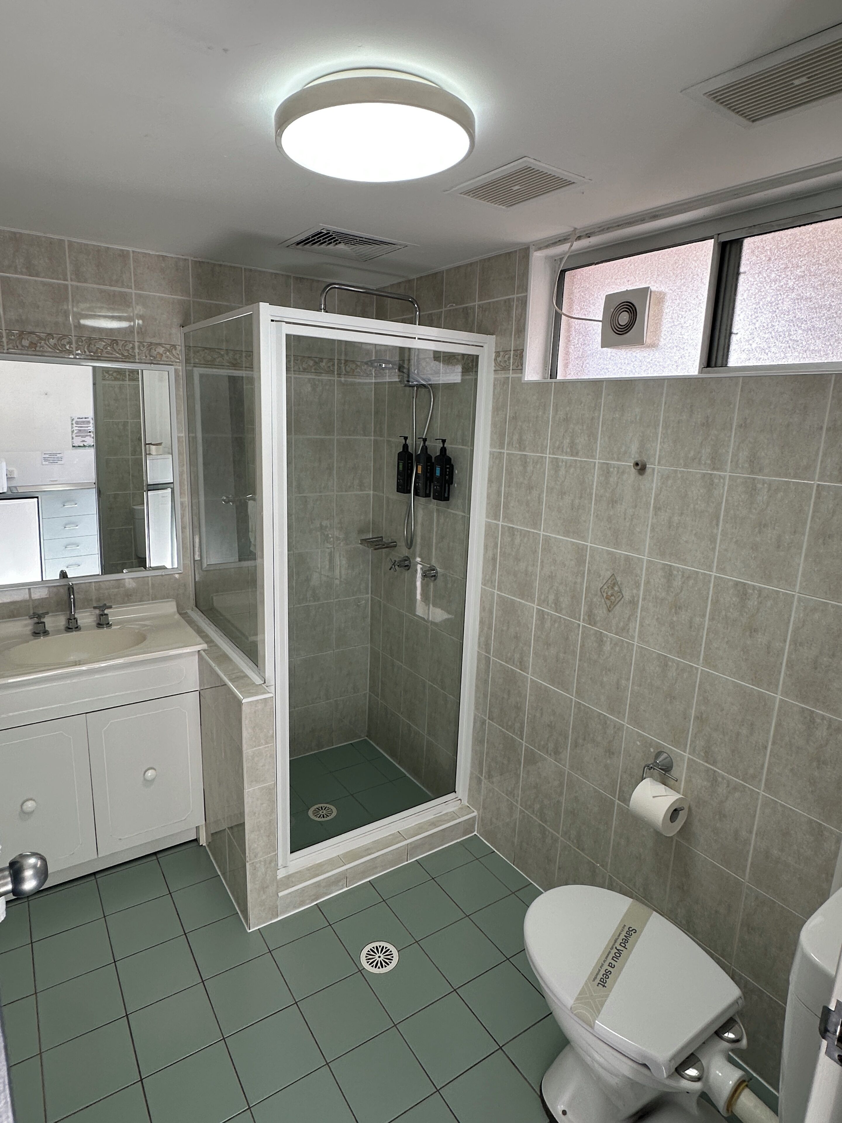 Un bany amb plat de dutxa, vàter i un lavabo amb mirall.