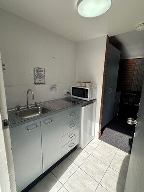 A compact kitchen with a sink, microwave, and cabinets. - The Oaks Hotel Motel (Albion Park Rail)