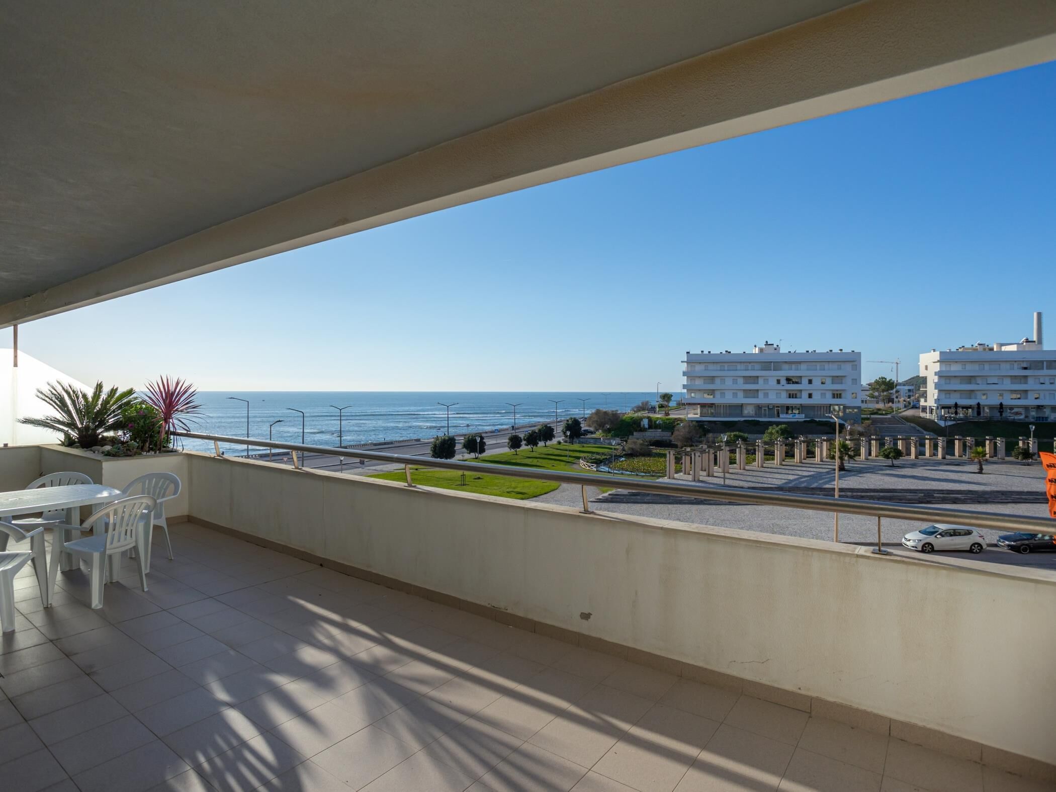Un balcón con vista al mar, una mesa con sillas y un edificio al fondo.