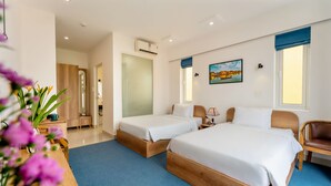 A hotel room with two beds, a desk, a chair, a vase with flowers, and a painting on the wall.