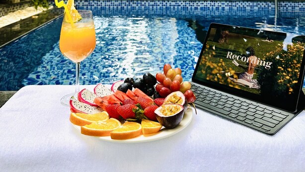 A poolside table with a drink, fruit, and a laptop displaying 'Recording'.