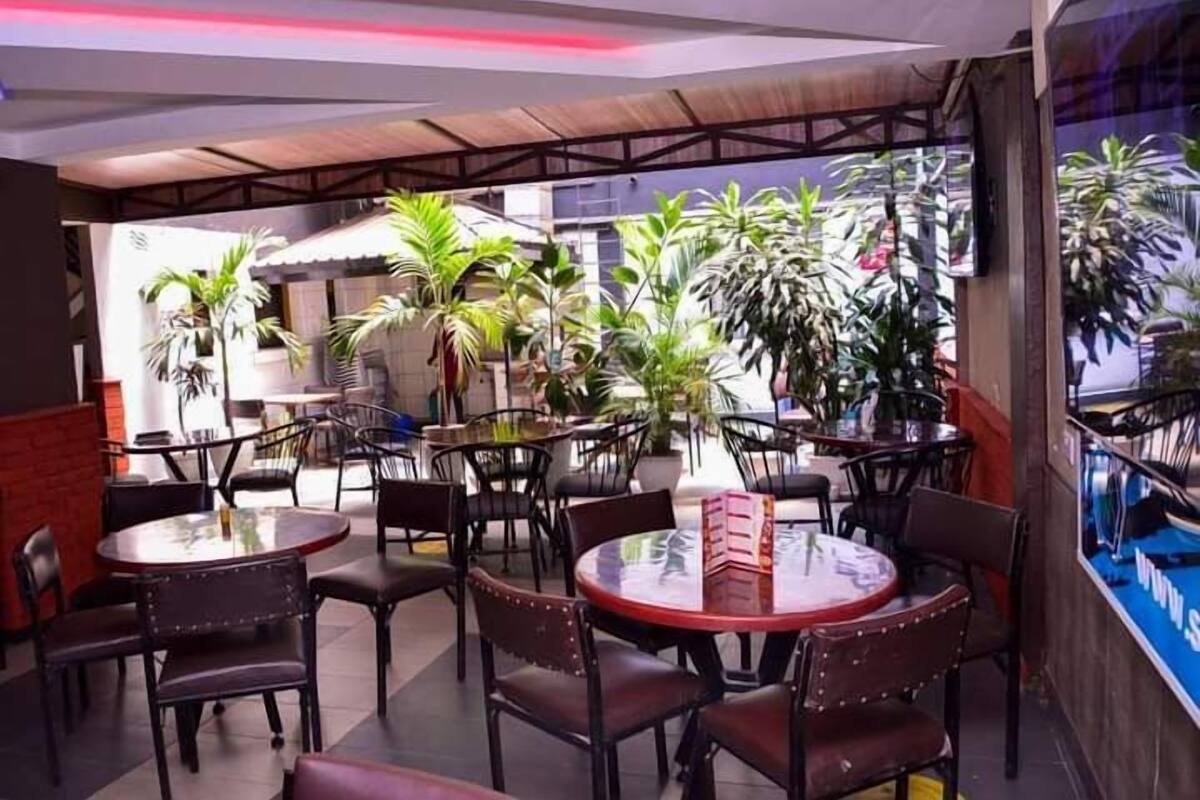 An indoor dining area with round tables and chairs, surrounded by potted plants.