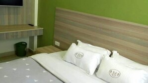 Un lit bien fait, avec une couvre-lit grise et des oreillers blancs, une tête de lit en bois, un mur vert et un téléviseur fixé au mur.