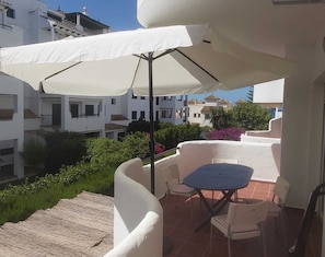 A balcony with a table and chairs, a white umbrella, and a view of neighboring buildings.