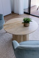 Una mesa redonda de madera con una planta en maceta encima, sobre una alfombra texturizada.