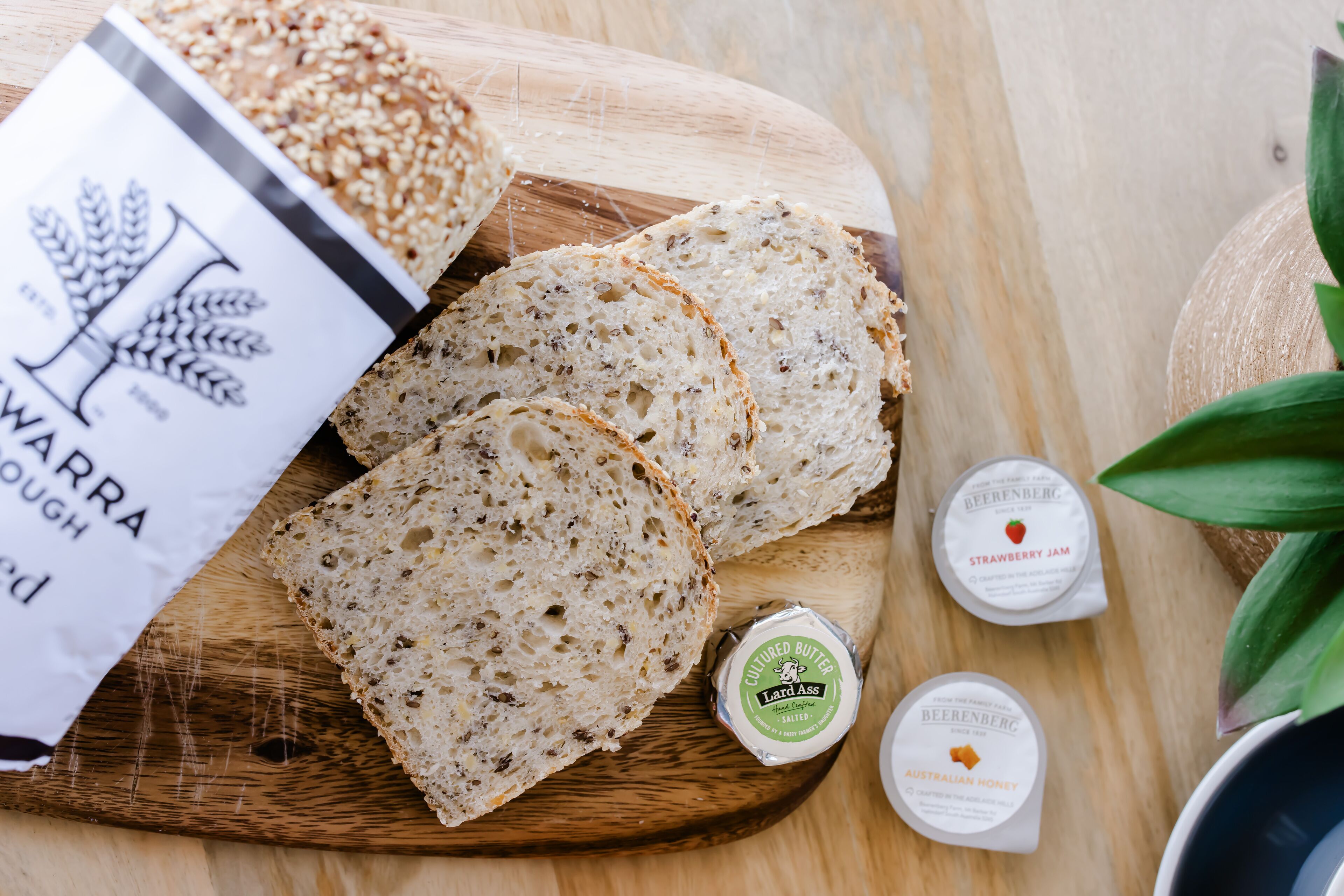 Skivefuld rugbrød på en træbræt, sammen med syltetøj og smør i glas.